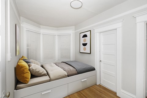 A white bedroom with a bed under a window and a picture on the wall.