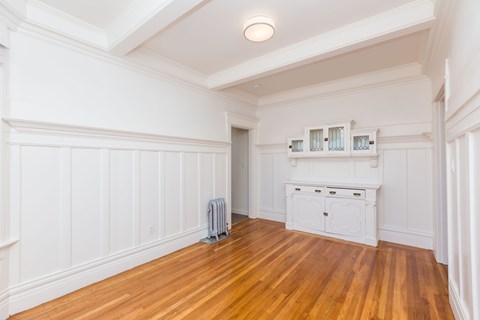 A room with white walls and wood flooring with a white cabinet and a radiator.