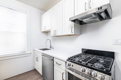 A white kitchen with a stove, sink, and cabinets.