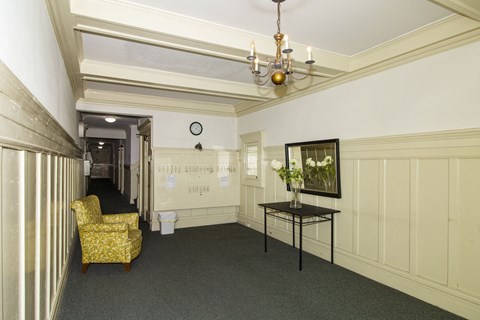 A yellow chair sits in a room with a chandelier and a painting on the wall.