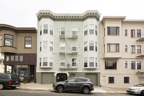 A car is parked in front of a building with a white balcony.