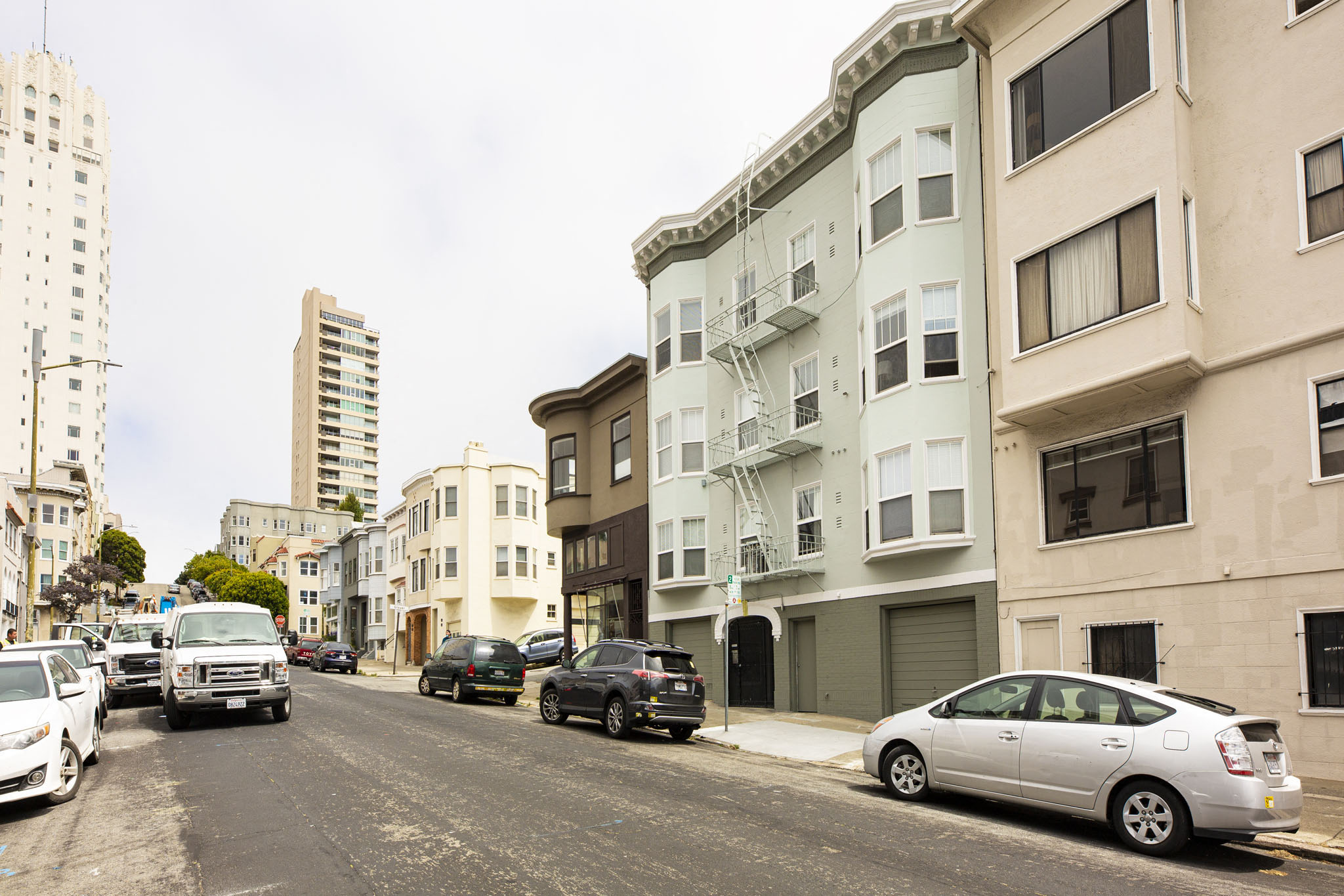 A street with cars parked on the side and buildings in the background.