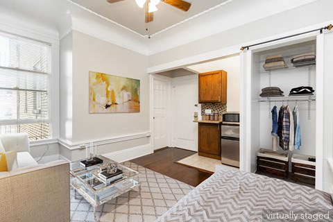 A spacious room with a ceiling fan, a painting on the wall, a coffee table, and a bed with a grey and white patterned bedspread.