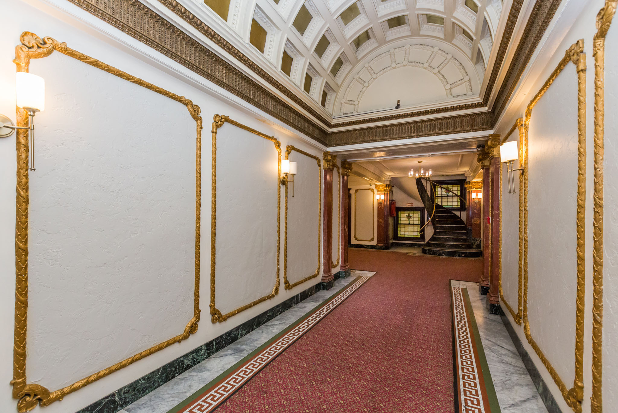 A hallway with a red carpet and gold trim.