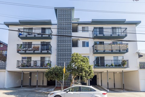 A white car is parked in front of a modern apartment building.