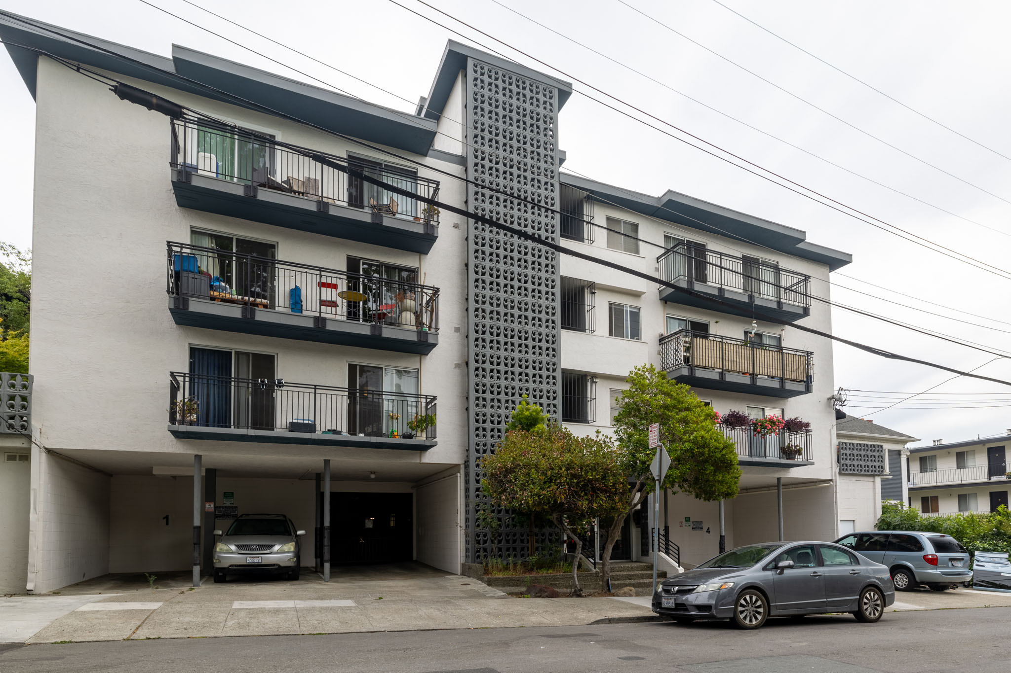 A white building with black balconies and a grey car parked in front.
