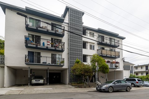 A white building with black balconies and a grey car parked in front.