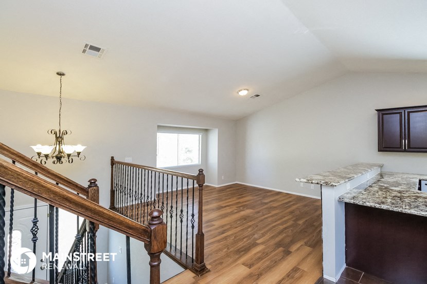 a living room with a staircase and a kitchen with wood floors