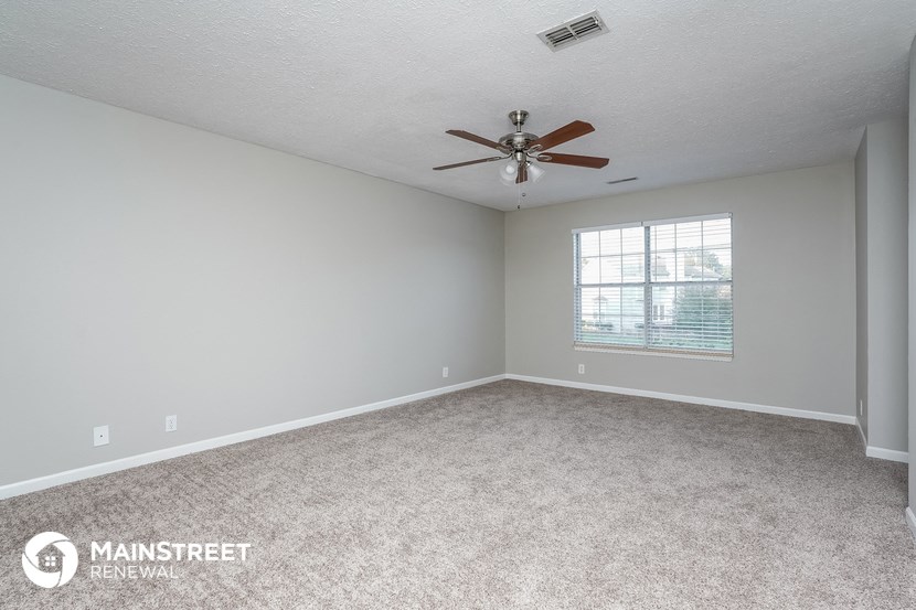 the spacious living room with ceiling fan and carpeting