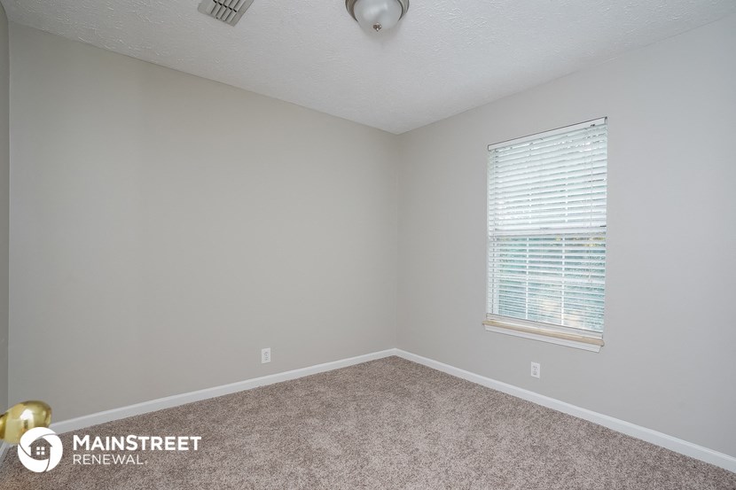the spacious bedroom with carpeted flooring and a window