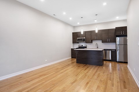 an empty living room and kitchen with wood flooring and stainless steel appliances