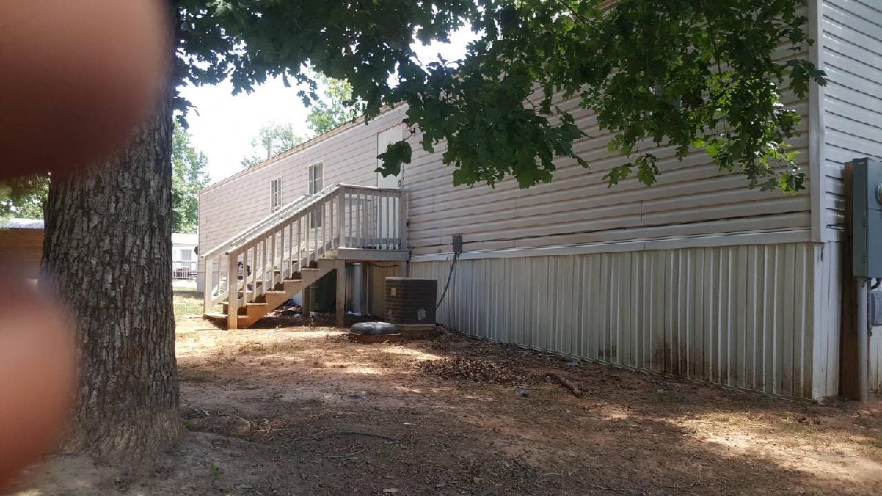 A tree is in the foreground of a photo showing a house with a garage.