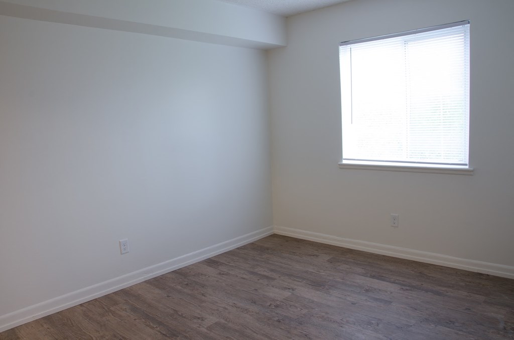a bedroom with white walls and wood floors and a window
