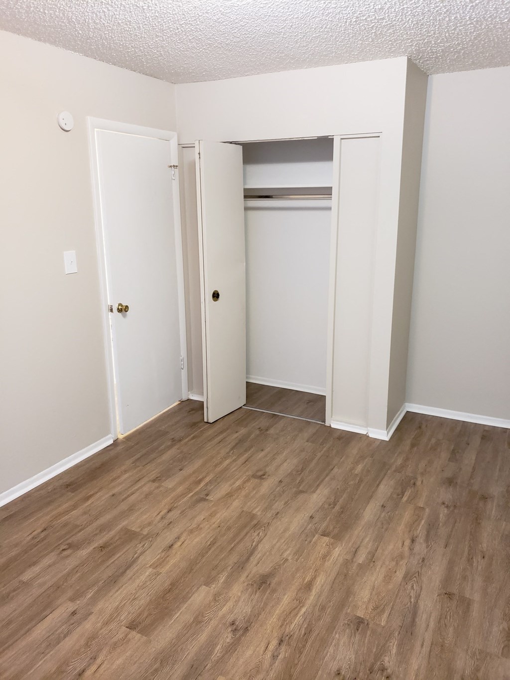 a bedroom with white walls and wood flooring and a closet