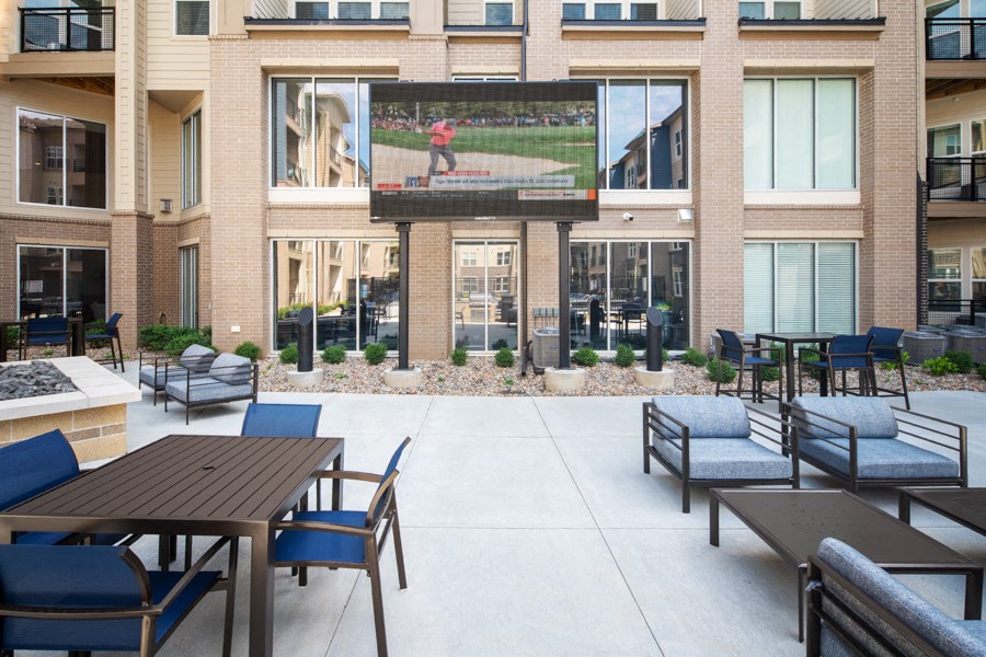 a patio with tables and chairs in front of a building with a tv on the