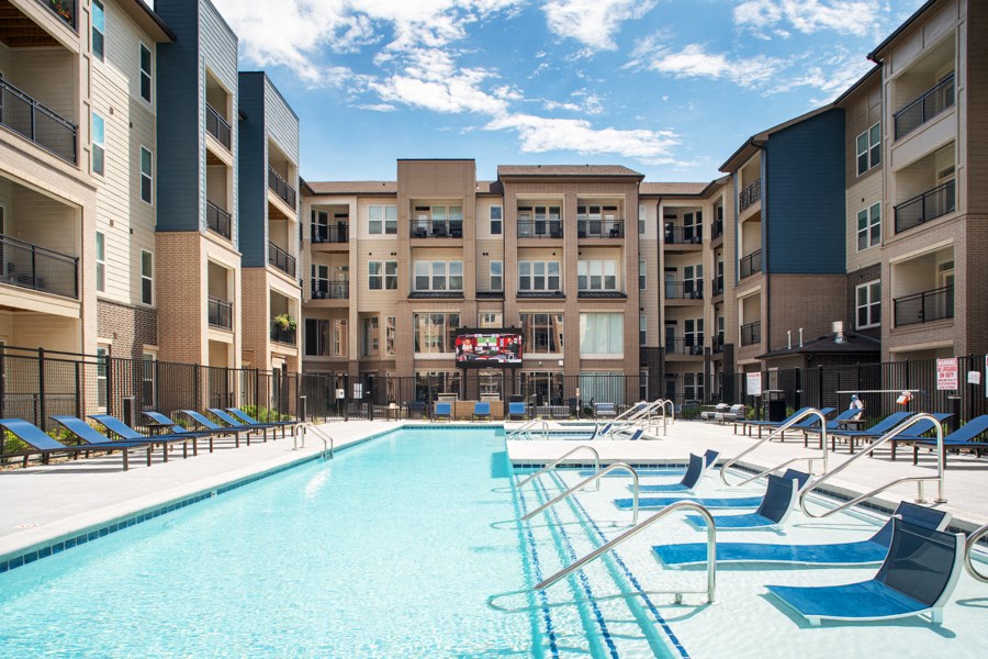 a pool with blue chairs and an apartment building in the background