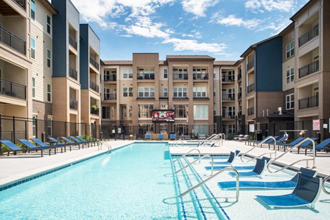 a pool with blue chairs and an apartment building in the background