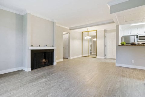 an empty living room with a fireplace and a kitchen