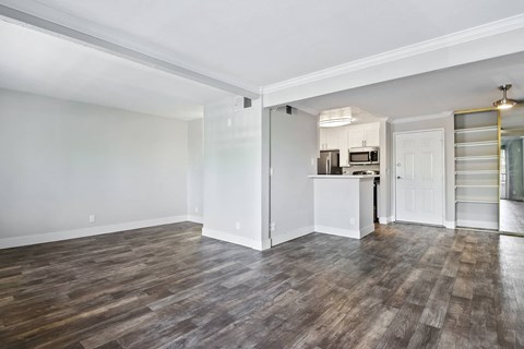 an empty living room with a kitchen in the corner