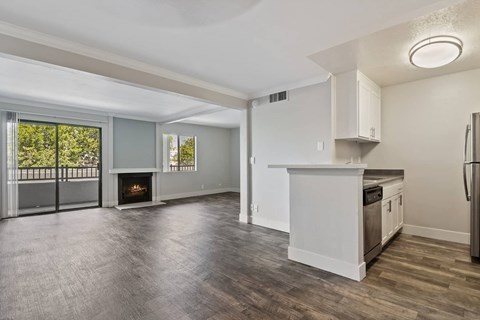 an empty living room with a kitchen and a fireplace