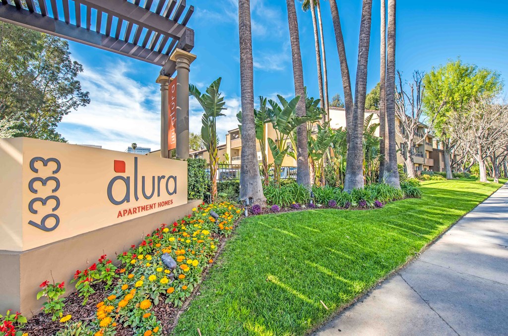 the entrance to the apartments sign with flowers and palm trees