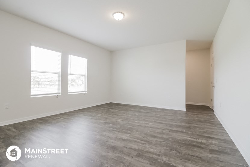 the spacious living room with white walls and wood flooring