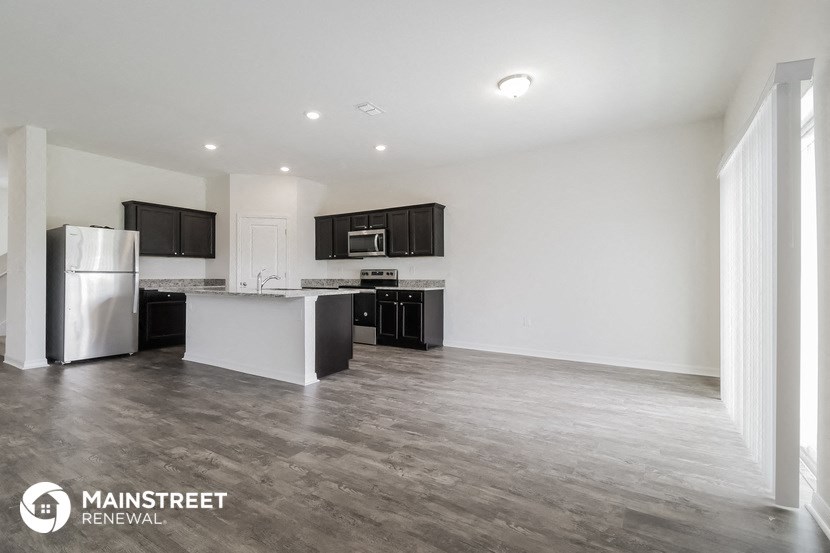 an empty living room with a kitchen with a refrigerator and