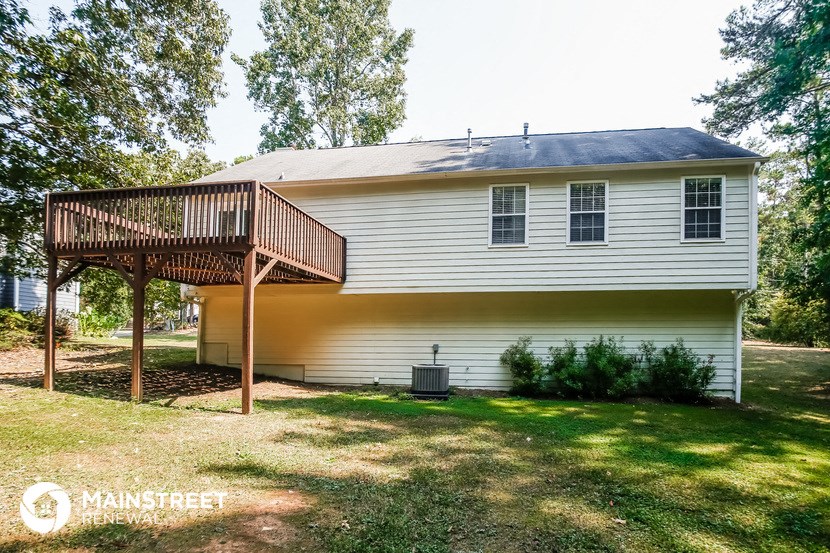 the back of a white house with a deck and a tree