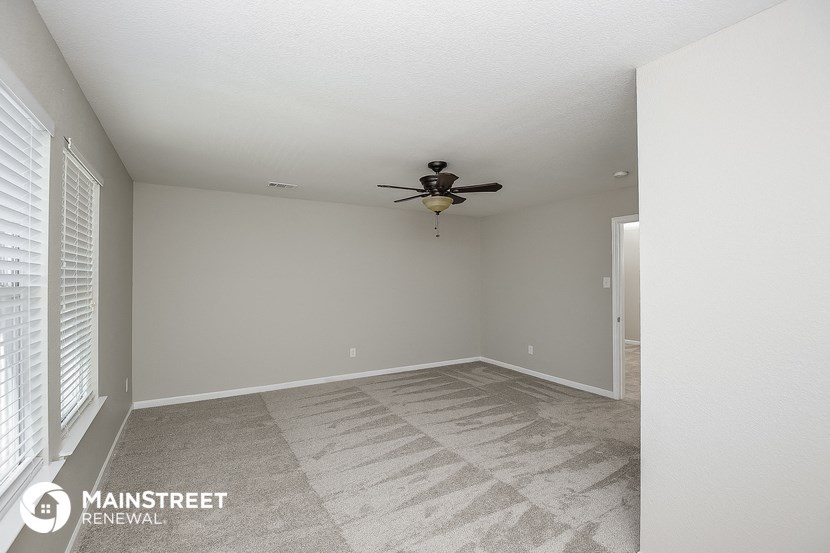 an empty living room with a ceiling fan and window