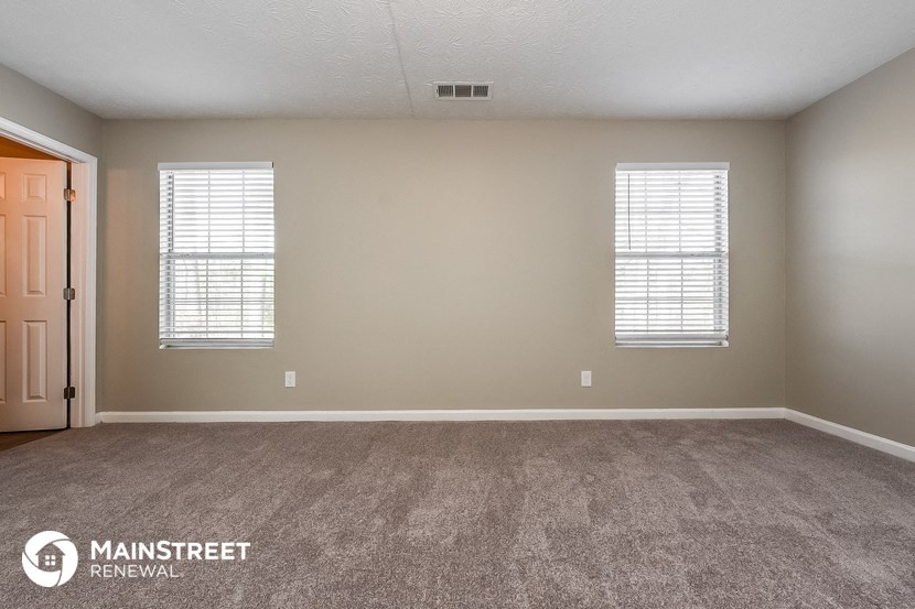 the spacious living room with carpeted flooring and two windows
