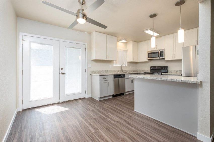 View of open kitchen with wood look flooring, stone counters, white cabinets, stainless appliances, ceiling fan, and lighting