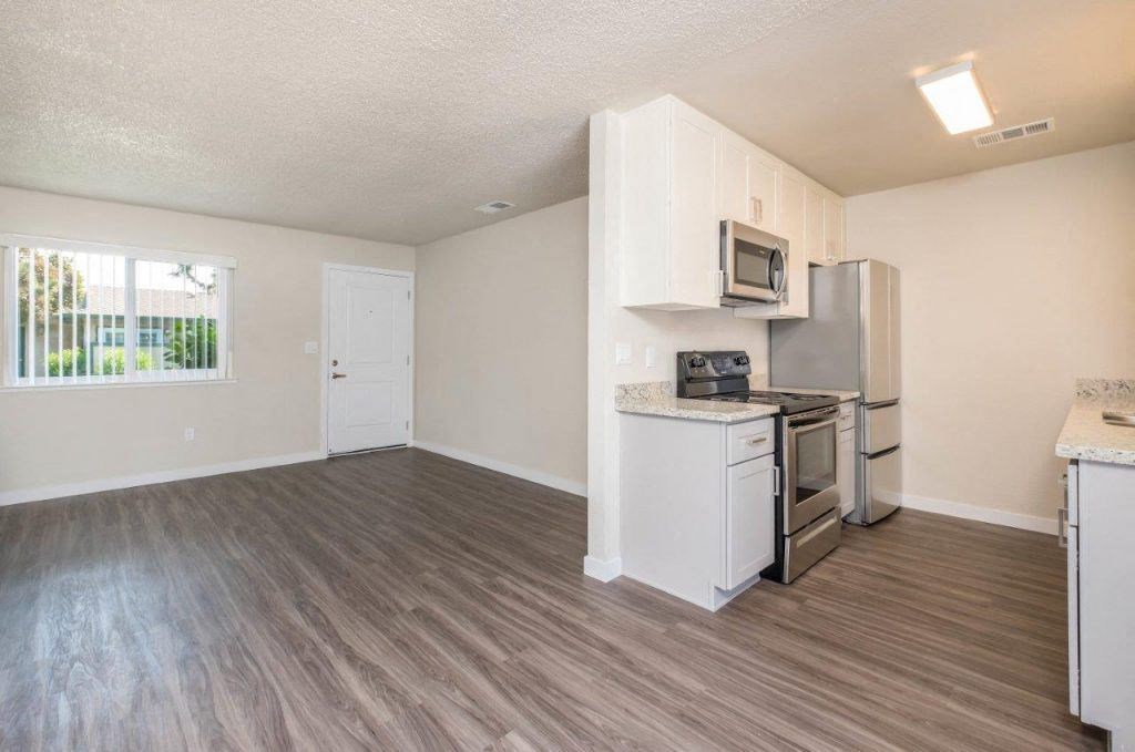 living and kitchen area View of living and kitchen area with wood look flooring, well lit window in living area, stone counters in kitchen, stainless appliances, and white cabinets.