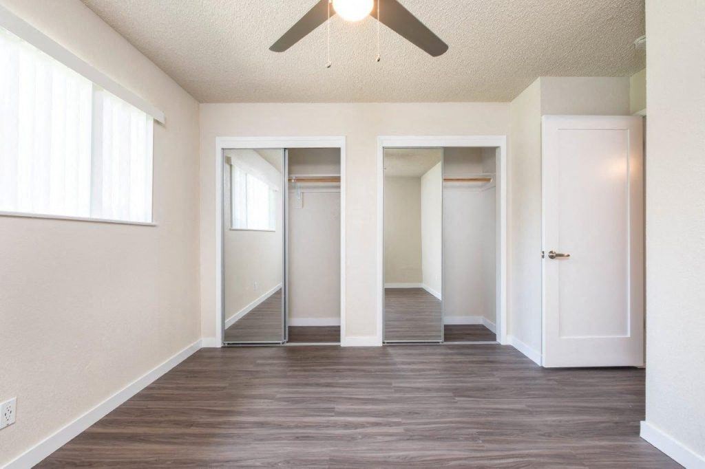 View from bedroom into sliding mirror door closet, has well lit window and ceiling fan
