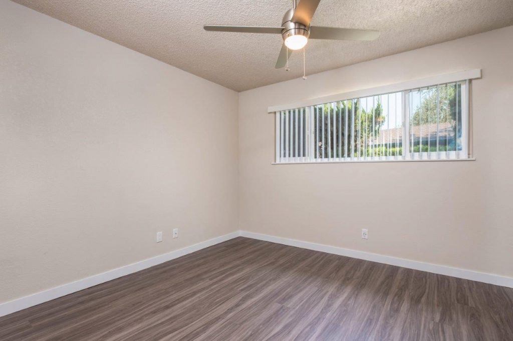 an empty living room with a window and a ceiling fan