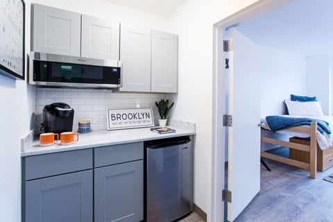 a kitchen with white cabinets and a sink and a microwave   and a bed