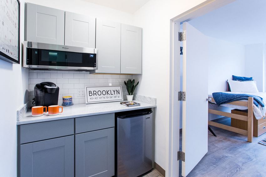a kitchen with white cabinets and a sink and a microwave and a bed