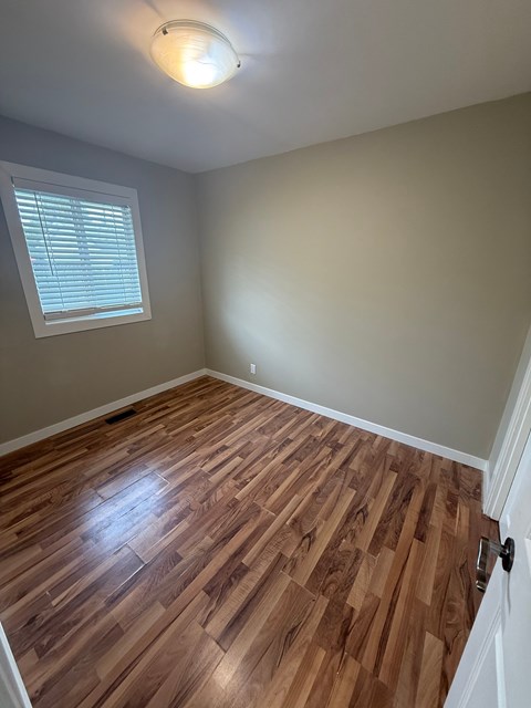 A room with wooden flooring and a window with blinds.