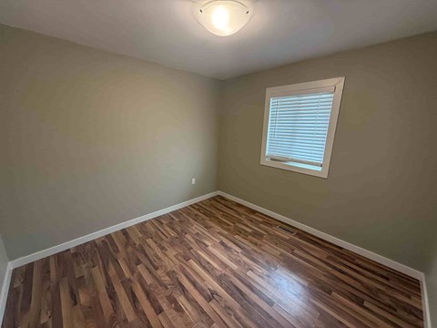 A room with wooden flooring and a window with blinds.