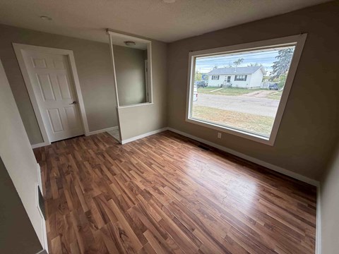 A room with wood flooring and a window showing a house outside.