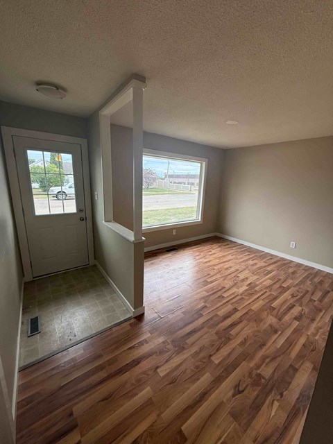 A room with wooden floors and a window overlooking a parking lot.