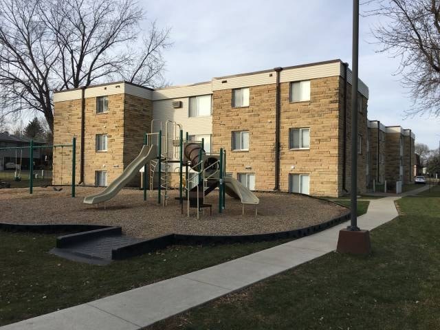 A playground with a slide and a building in the background.
