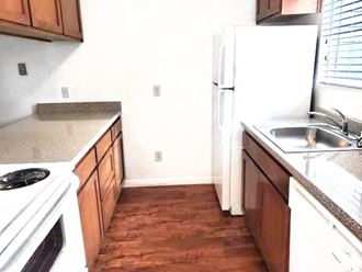 Galley kitchen with wood cabinets, vinyl flooring, oven, refrigerator, sink, and dishwasher
