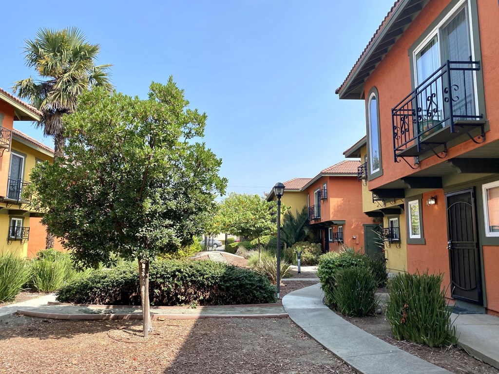 a walkway between two buildings with trees and bushes