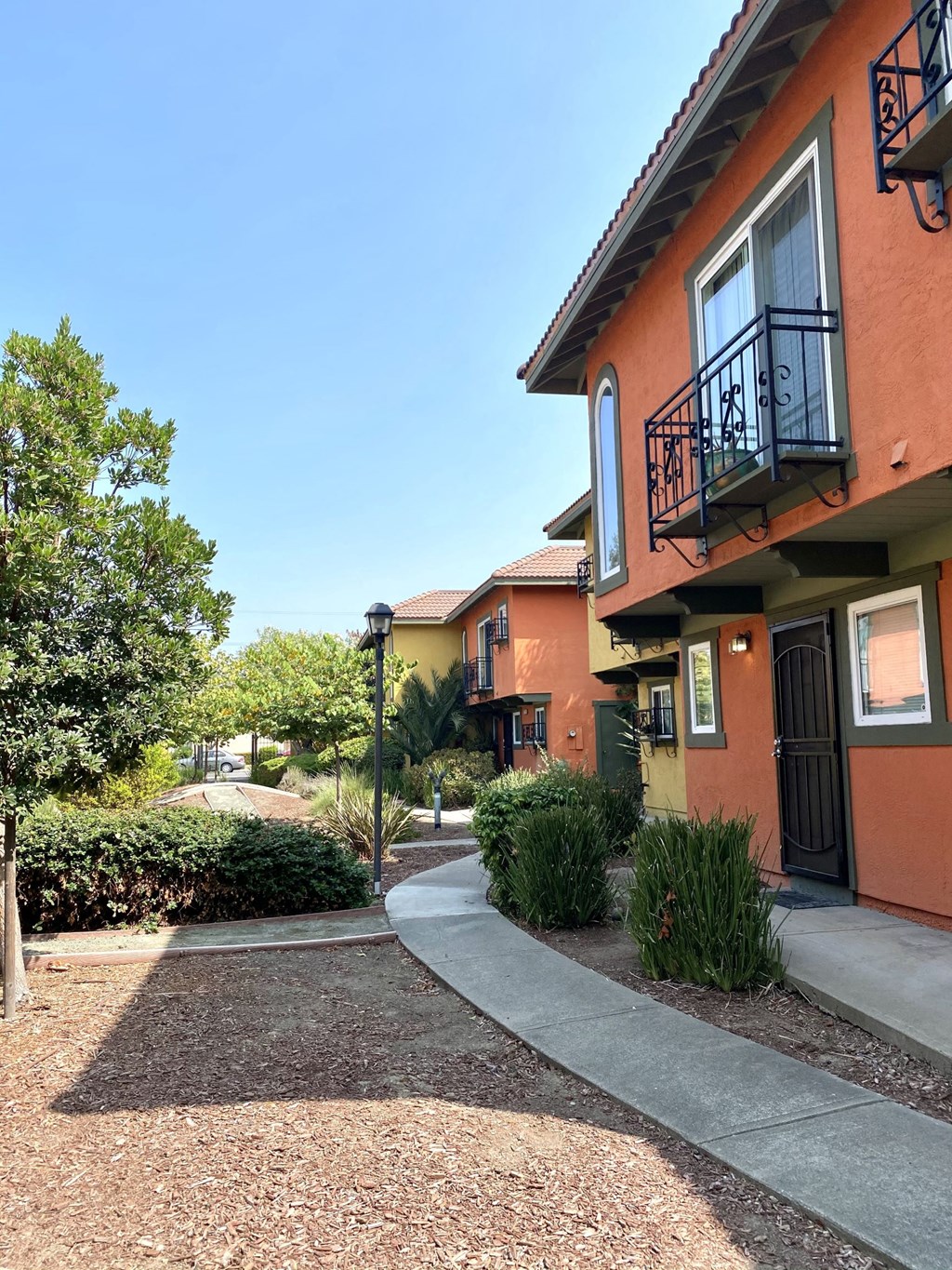 a sidewalk in front of a building with trees and bushes