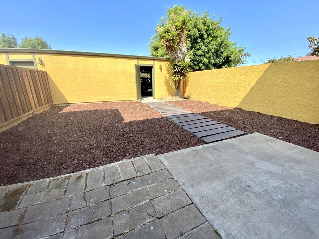 a yard with a yellow wall and a concrete walkway
