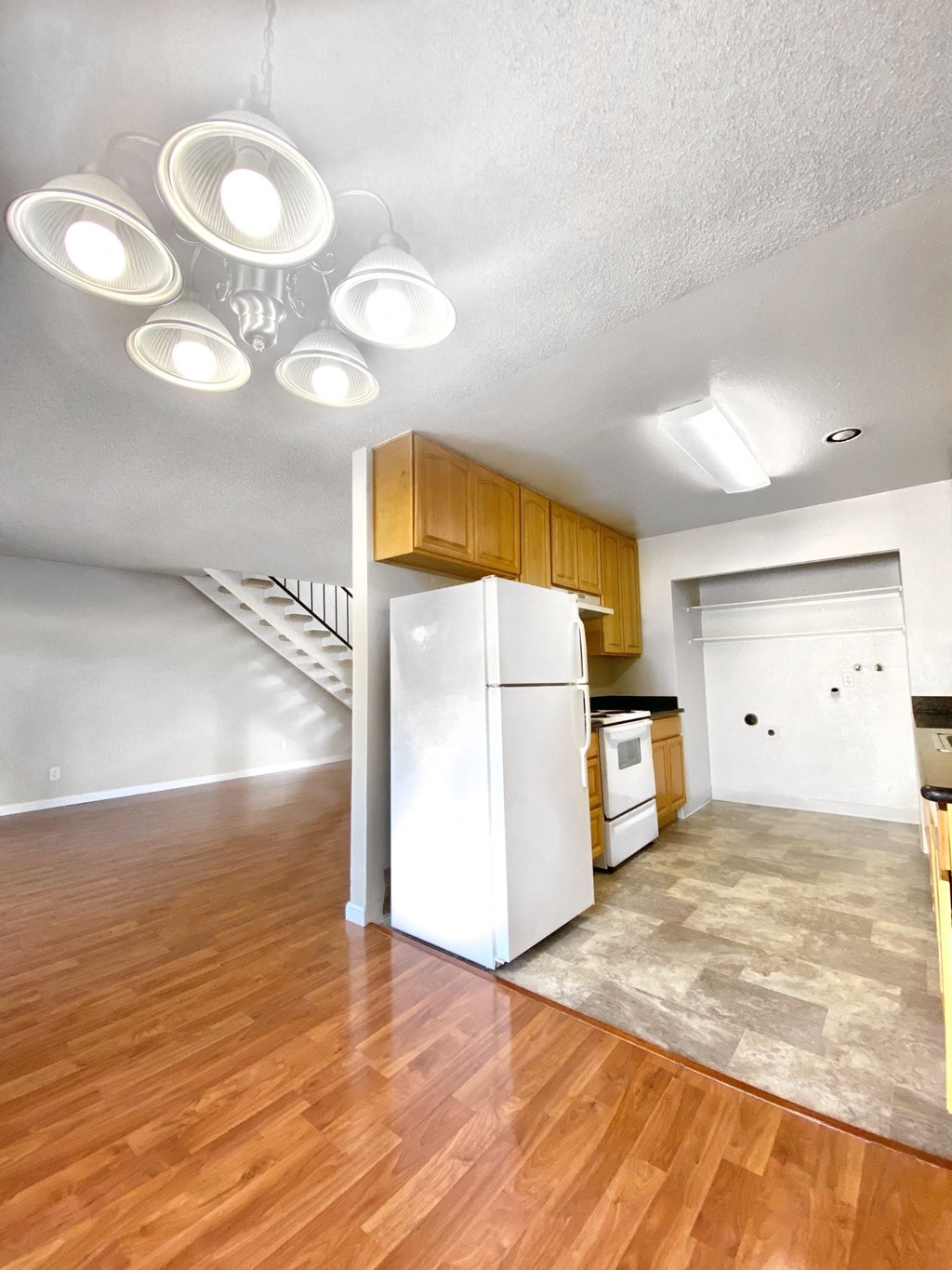 an empty living room with a kitchen and a refrigerator
