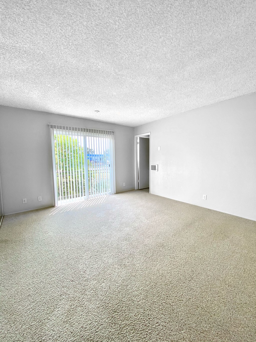 an empty living room with a sliding glass door to a balcony