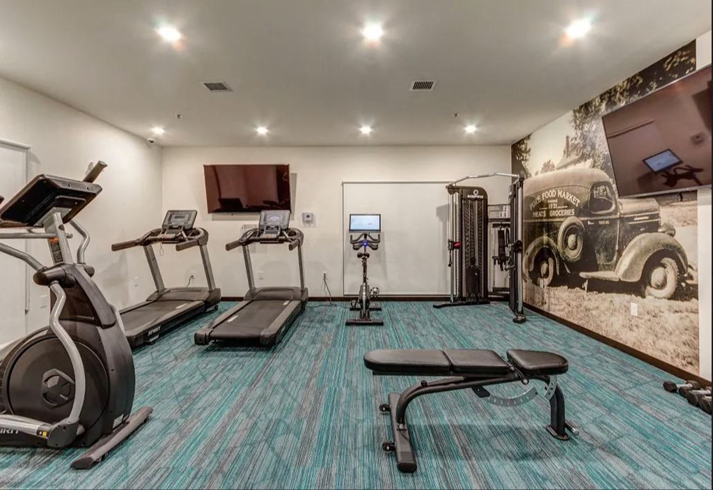 a gym with exercise equipment and a wall mural of an old car