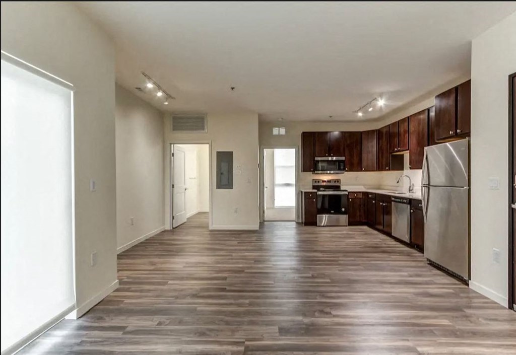an empty kitchen and living room with wooden floors and stainless steel appliances