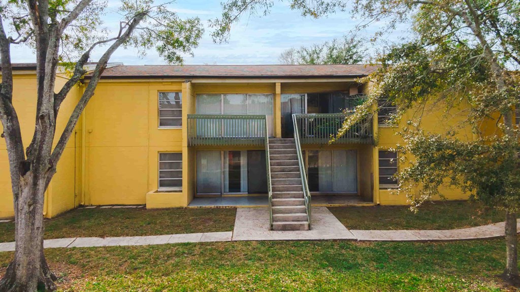 front view of a yellow house with a staircase and a tree